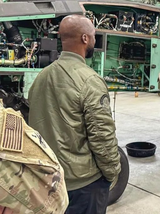 Person wearing a green jacket with a patch in front of an aircraft engine in USA
