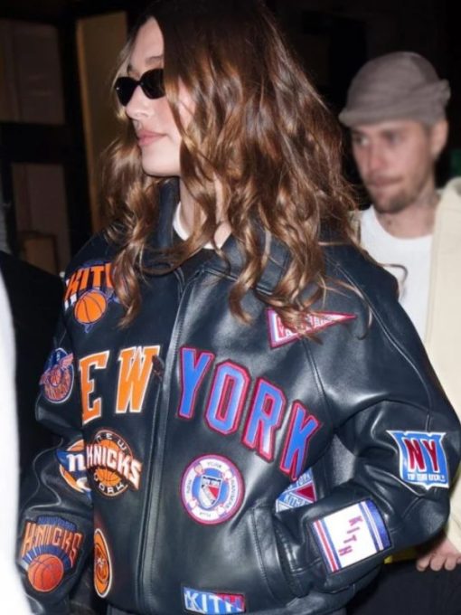 Person wearing a black leather jacket with 'New York' and sports team logos.