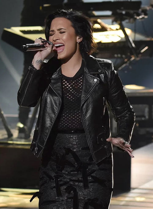 Person in black leather jacket and outfit singing on stage with musical instruments in the background